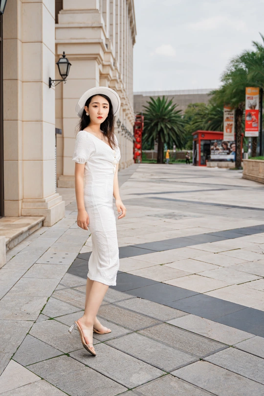 一位穿着白色连衣裙和帽子 沿着人行道走下的年轻女子