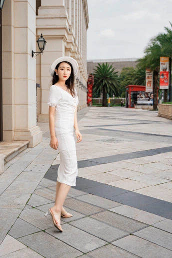一位穿着白色连衣裙和帽子 沿着人行道走下的年轻女子