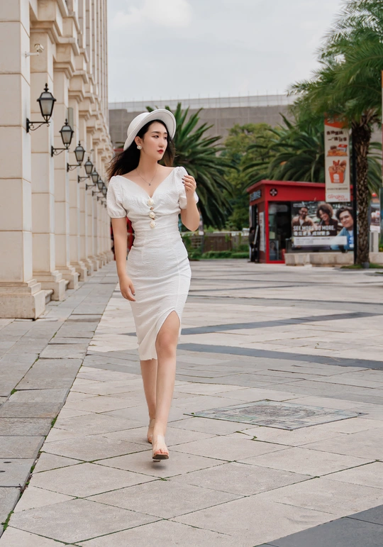 一位穿着白色连衣裙和帽子在人行道上行走的年轻女子