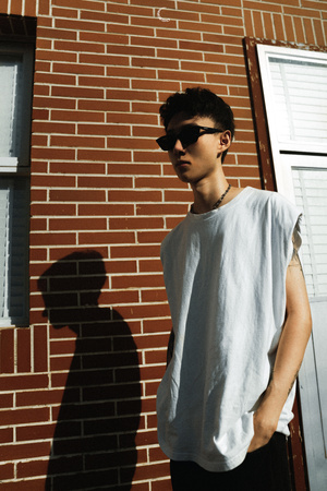 一个戴着墨镜、穿着白色t恤的年轻人站在一堵有窗户和门的砖墙前的滑板上