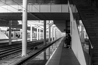 一张黑白照片 车站站台上有一个人站着 平台上有人走下来。