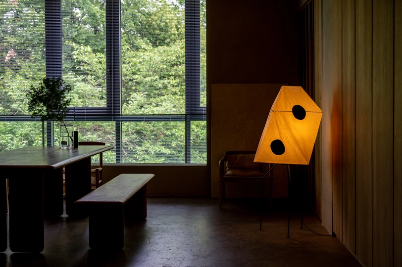 一个带有大窗户的房间 一张带有椅子的桌子 一张长凳和一盏黄色的灯。