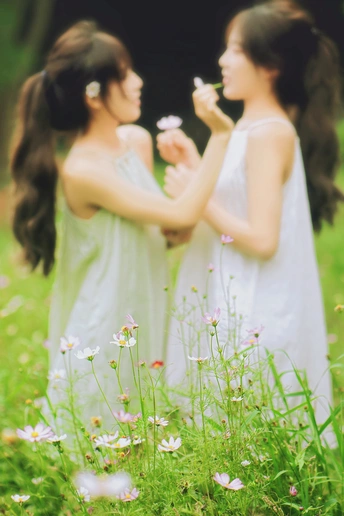 两个穿着白色连衣裙的年轻女子在田里手捧鲜花