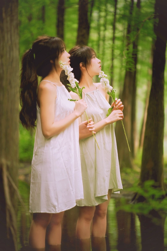 一对身穿白色连衣裙、手捧鲜花的年轻男女站在树林里