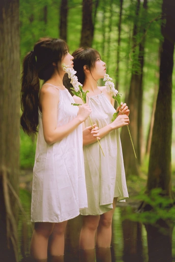 一对身穿白色连衣裙、手捧鲜花的年轻男女站在树林里