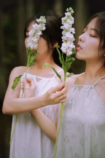 一个年轻的女人在森林里闻着白花