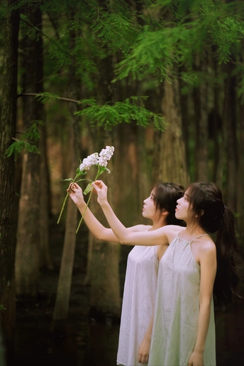 一位身穿白色连衣裙、手捧鲜花的年轻女子站在树林里