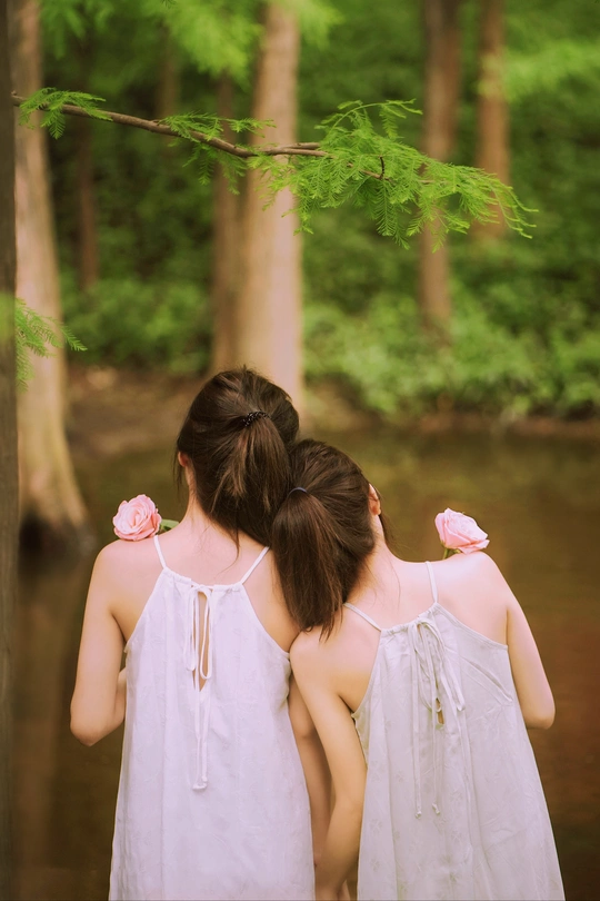 两个穿着白色连衣裙的年轻女人站在树林里的小溪里