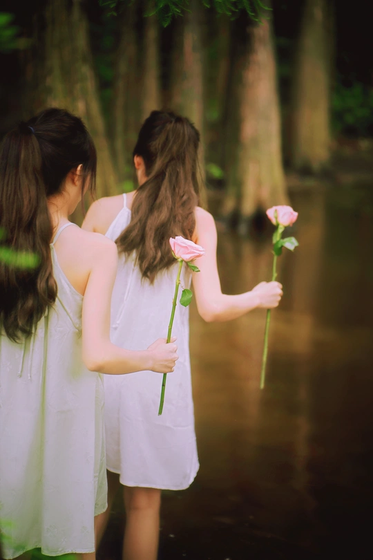 两个穿着白色连衣裙、手里拿着粉色玫瑰的年轻女子站在水中