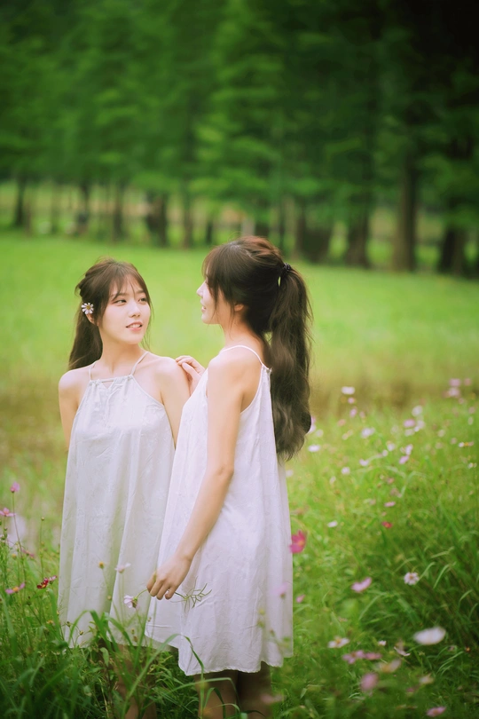 两个穿着白色连衣裙的小女孩站在一片草地和鲜花中