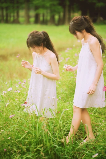 两个穿着白色连衣裙的小女孩在草地上采花