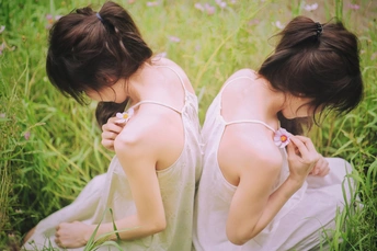 两个穿着白色连衣裙的年轻女人坐在高高的绿草地里