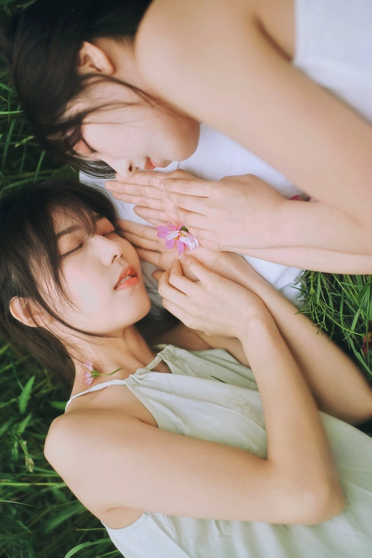 一个手里拿着花的年轻女人和一个躺在草地上的小女孩