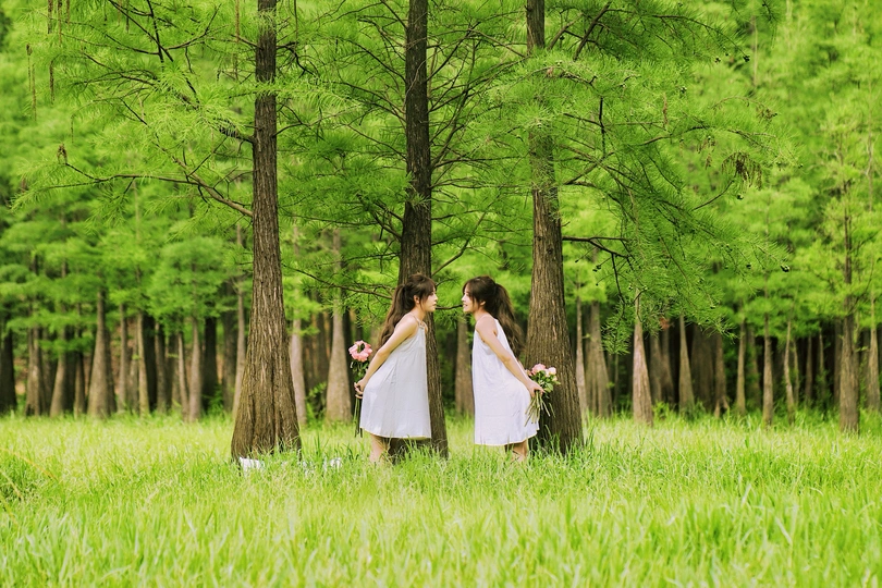 一个穿着白色连衣裙的女人抱着一个穿着白裙子的小女孩站在草地和树林里