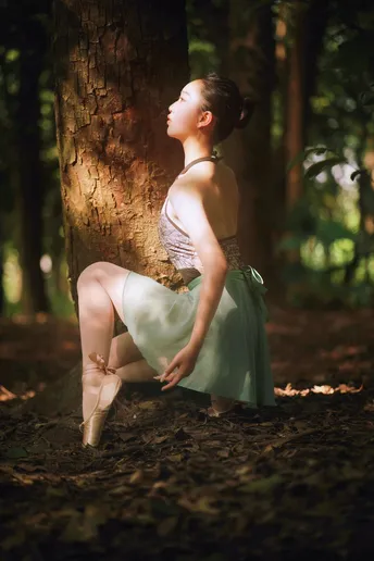 一位年轻女子穿着一件美丽的裙子坐在树林中的一棵树上