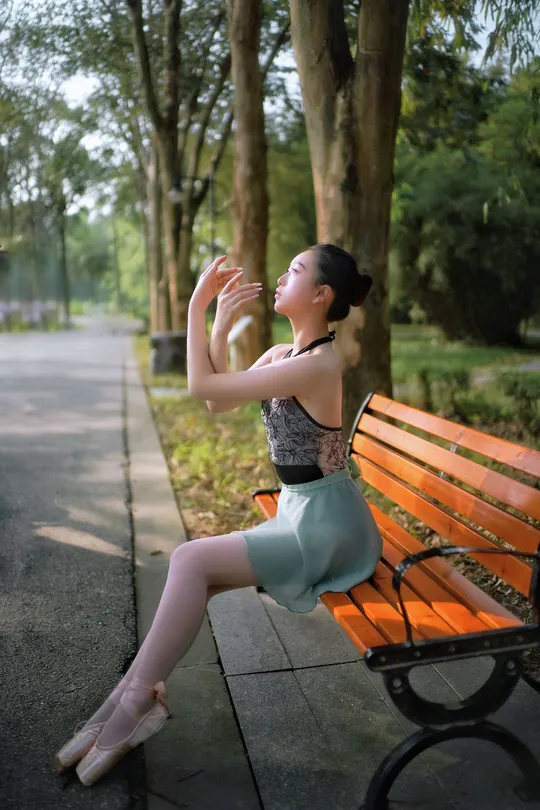 一位穿着芭蕾舞裙的年轻女子坐在公园的长椅上。