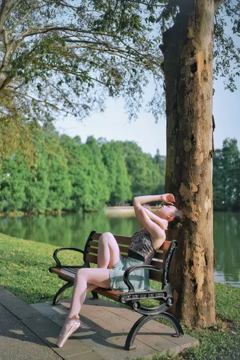 一个人躺在公园里的一张长椅上 靠近一棵树和水体。