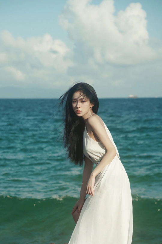 一位长发白衣少女站在海滩附近的水边