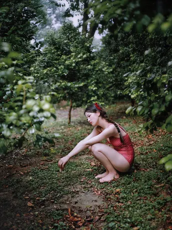 一位穿着红裙子的年轻女子坐在果园里