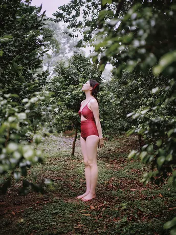 一位穿着红衣服的年轻女子站在森林中的果园里 树上结满了苹果。