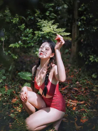 一位穿着红色的年轻女子在森林中摆姿势 脸上有蕨类植物。
