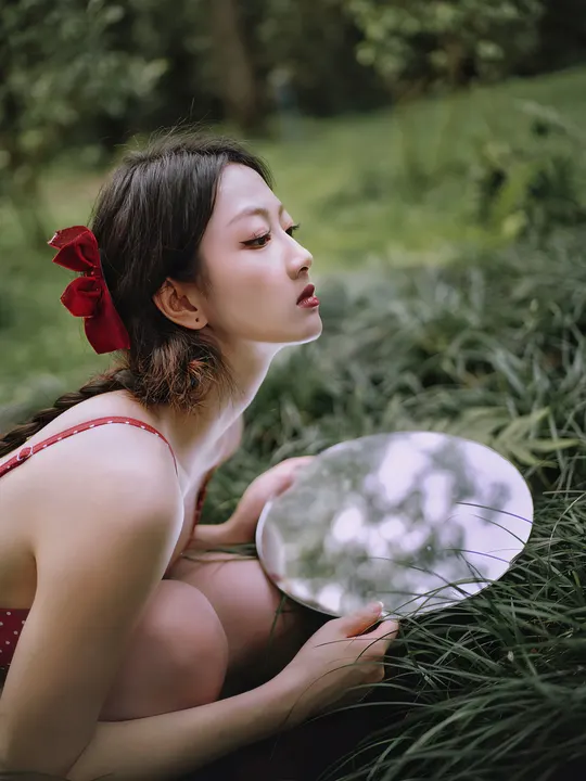 一个穿着红裙子的年轻女子坐在草地上 手里拿着一盘白盘子。