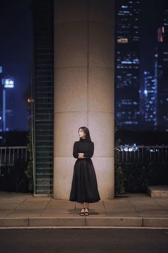 一位穿着黑色连衣裙的女人站在夜晚的街道上 前面有一栋建筑。