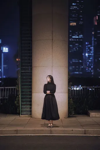 一位穿着黑色连衣裙的女人站在夜晚的街道上 前面有一栋建筑。