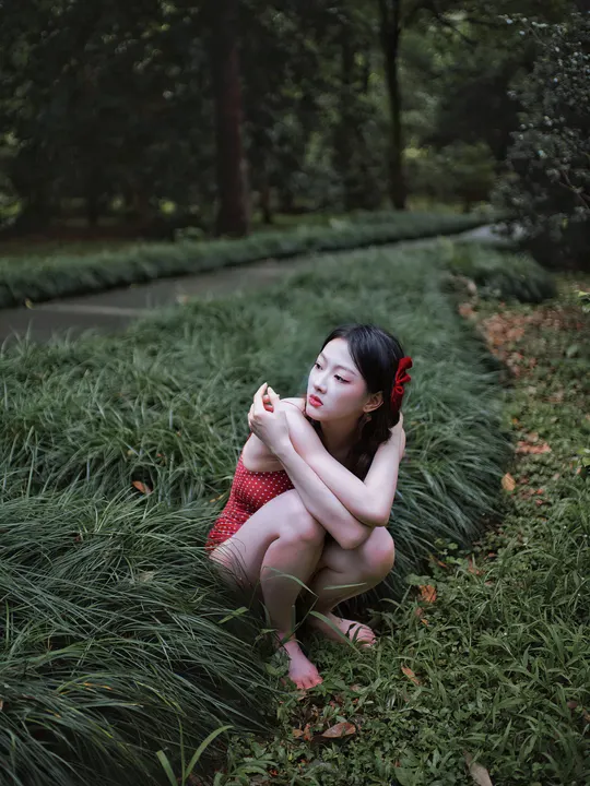 一个穿着红裙子的年轻女子坐在公园里的 tall grass 中。