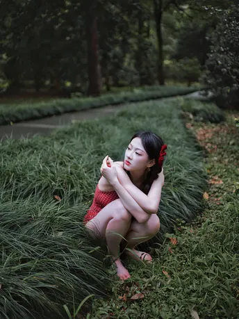 一个穿着红裙子的年轻女子坐在公园里的 tall grass 中。