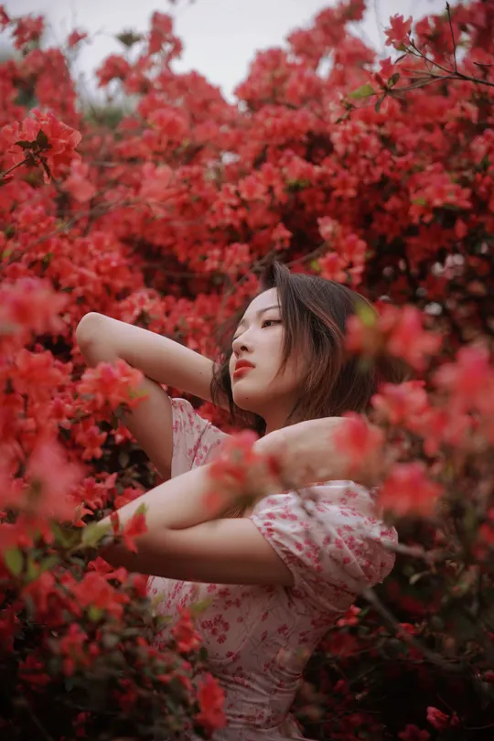 一个穿着粉红色连衣裙的年轻女子站在一片红色的花朵之中。