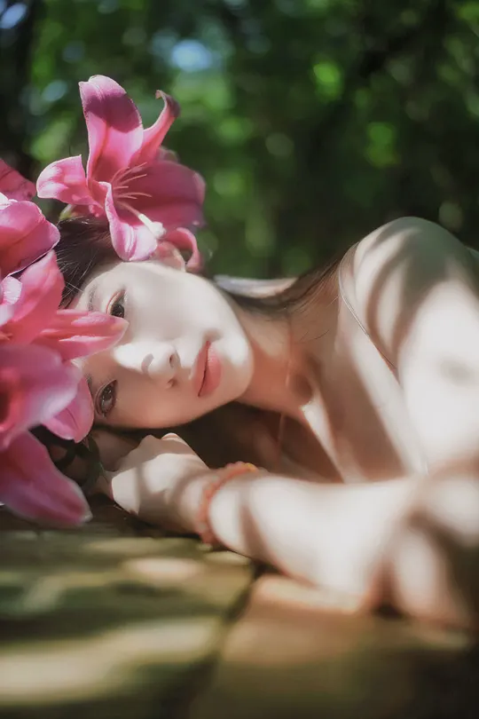 一个穿着粉红色连衣裙的美丽年轻女子躺在地上 周围有粉红色花朵。