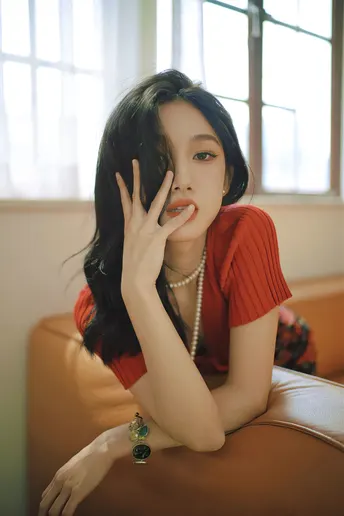 一位穿着红衬衫的年轻女子坐在棕色沙发上 手扶着椅子的扶手。