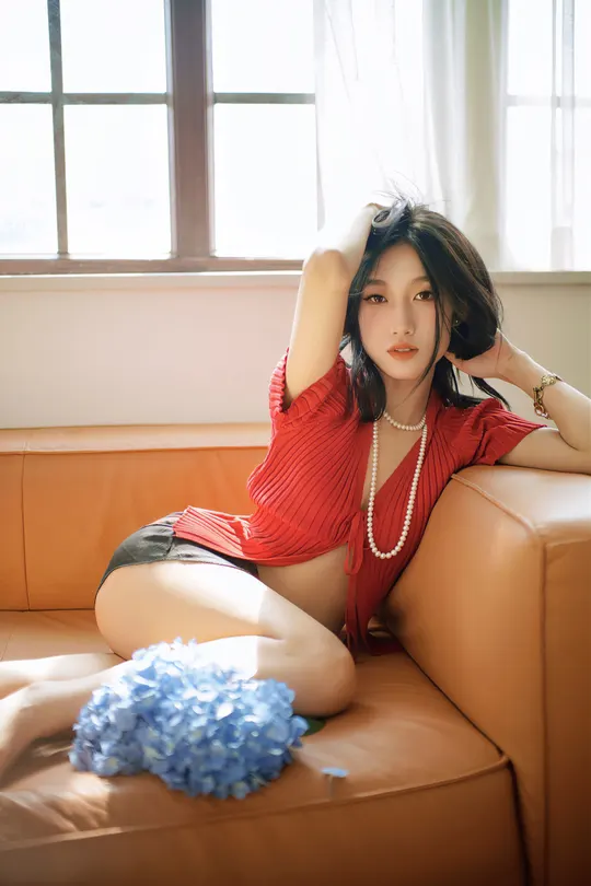 一个穿着红衬衫的年轻女子坐在一个棕色的沙发上 面对窗户。