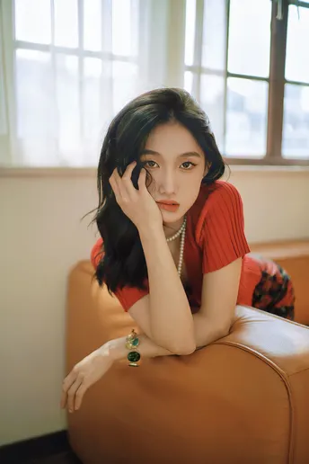 一个穿着红衬衫的年轻女子坐在棕色沙发上 身着红裙 站在窗户前。