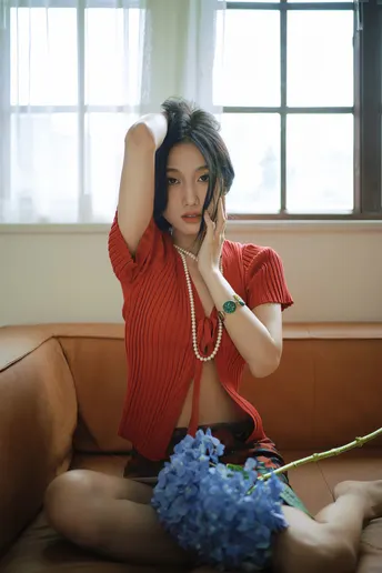 一个穿着红裙子的年轻女子坐在沙发上 手里拿着一束蓝色花。