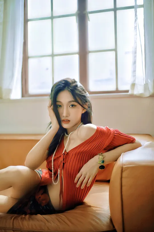 一个穿着红裙子的年轻女子坐在一个带有窗户的房间里的一张沙发上