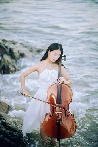 一位穿着白色连衣裙的年轻女子在靠近海洋的海滩上演奏小提琴