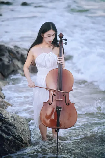 一个穿着白裙子的年轻女子在海洋附近的海滩上弹奏小提琴 手持一把美丽的小提琴 站在水中。