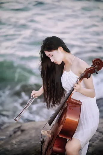 一位穿着白色连衣裙的年轻女子在海洋或水边的沙滩上演奏小提琴