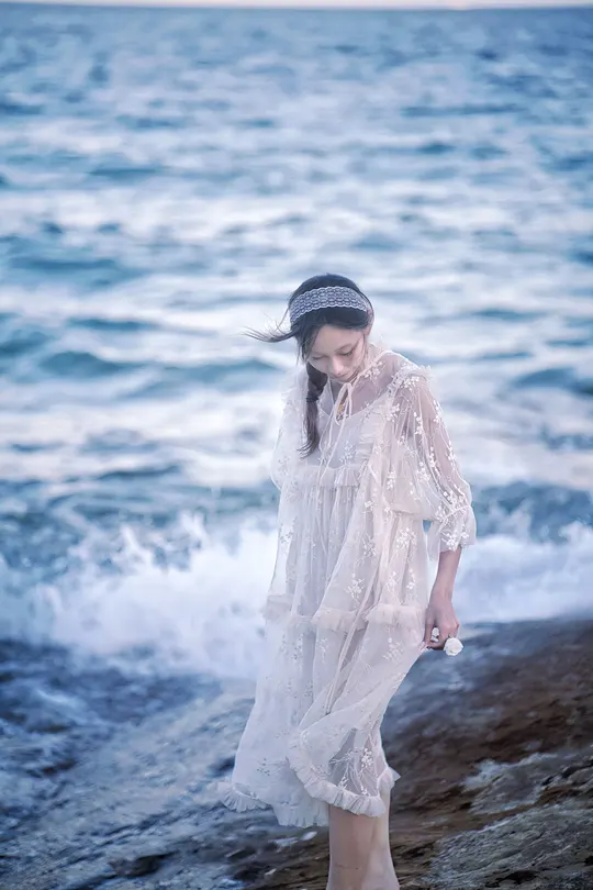 一位穿着白色连衣裙的年轻女子沿着靠近海洋的海滩散步