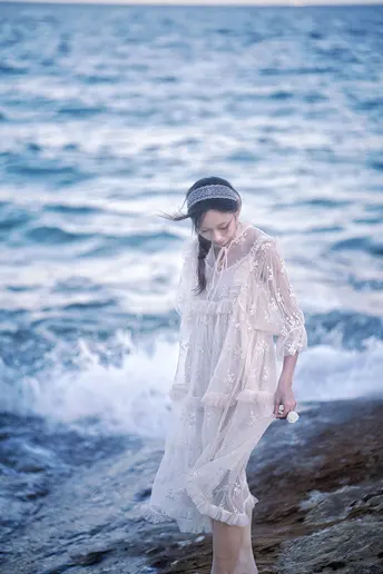 一位穿着白色连衣裙的年轻女子沿着靠近海洋的海滩散步