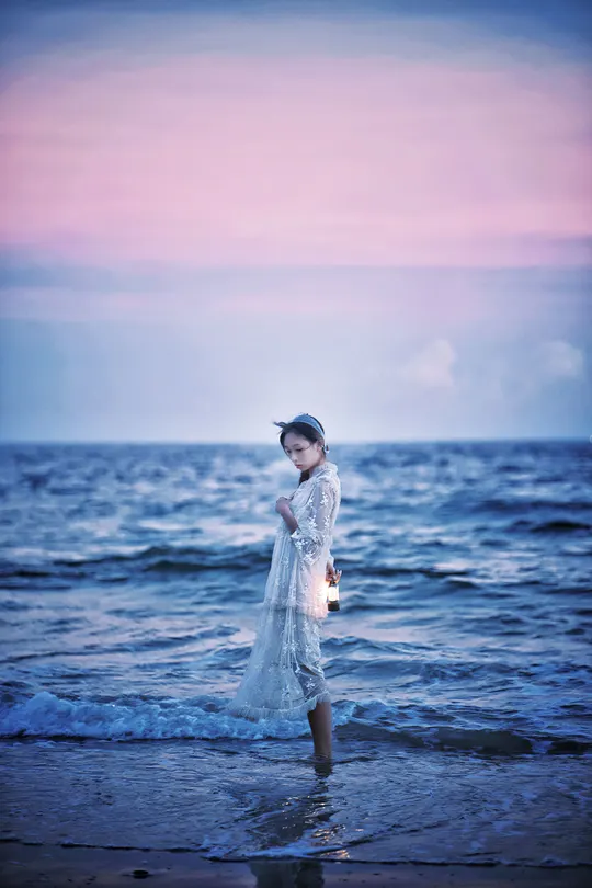 一个小女孩穿着白色裙子站在海滩上的水中