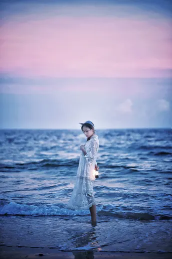 一个小女孩穿着白色裙子站在海滩上的水中