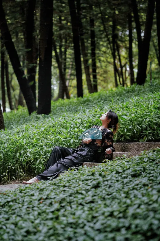 一位妇女躺在绿森林中的一张长椅上 而一位带着雨伞的男人躺在草地上。