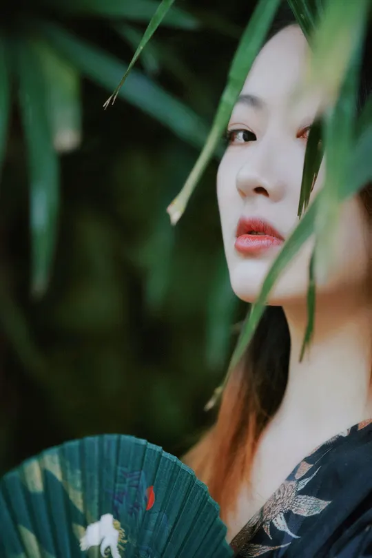 一位穿着和服的女孩拿着一把扇子 扇子上有一个红色的花。