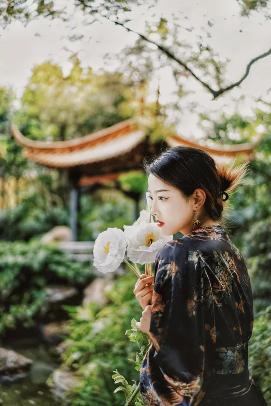 一位穿着和服的年轻女子 闻着白色花朵的香气。