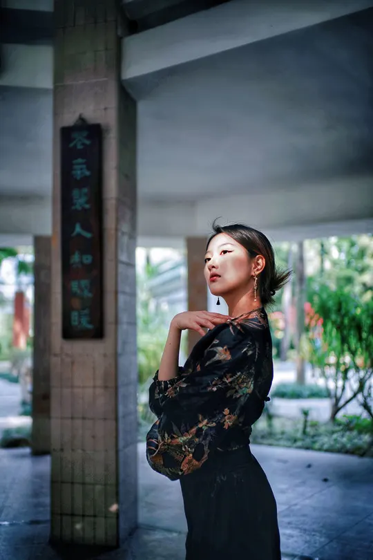 一个穿着黑色连衣裙的年轻女子站在一把伞下