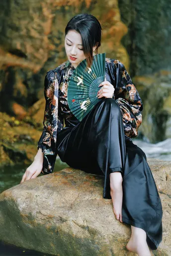 一位穿着和服的女士拿着扇子坐在岩石上
