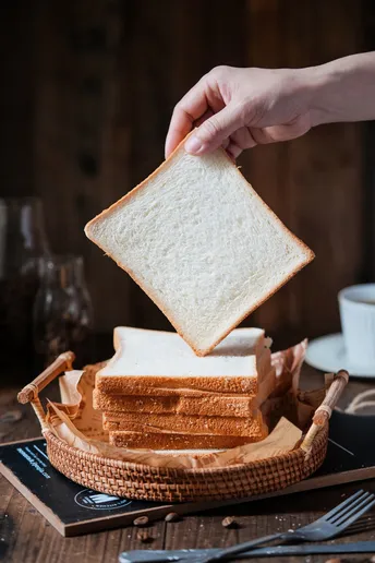 一个人正在桌子上的篮子里拿三明治 盘子里装着切好的cheese。